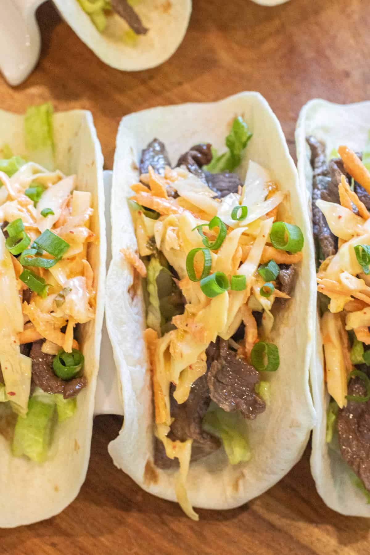 an overhead of 3 tacos in a taco holder with beef, slaw, and green onions on top.