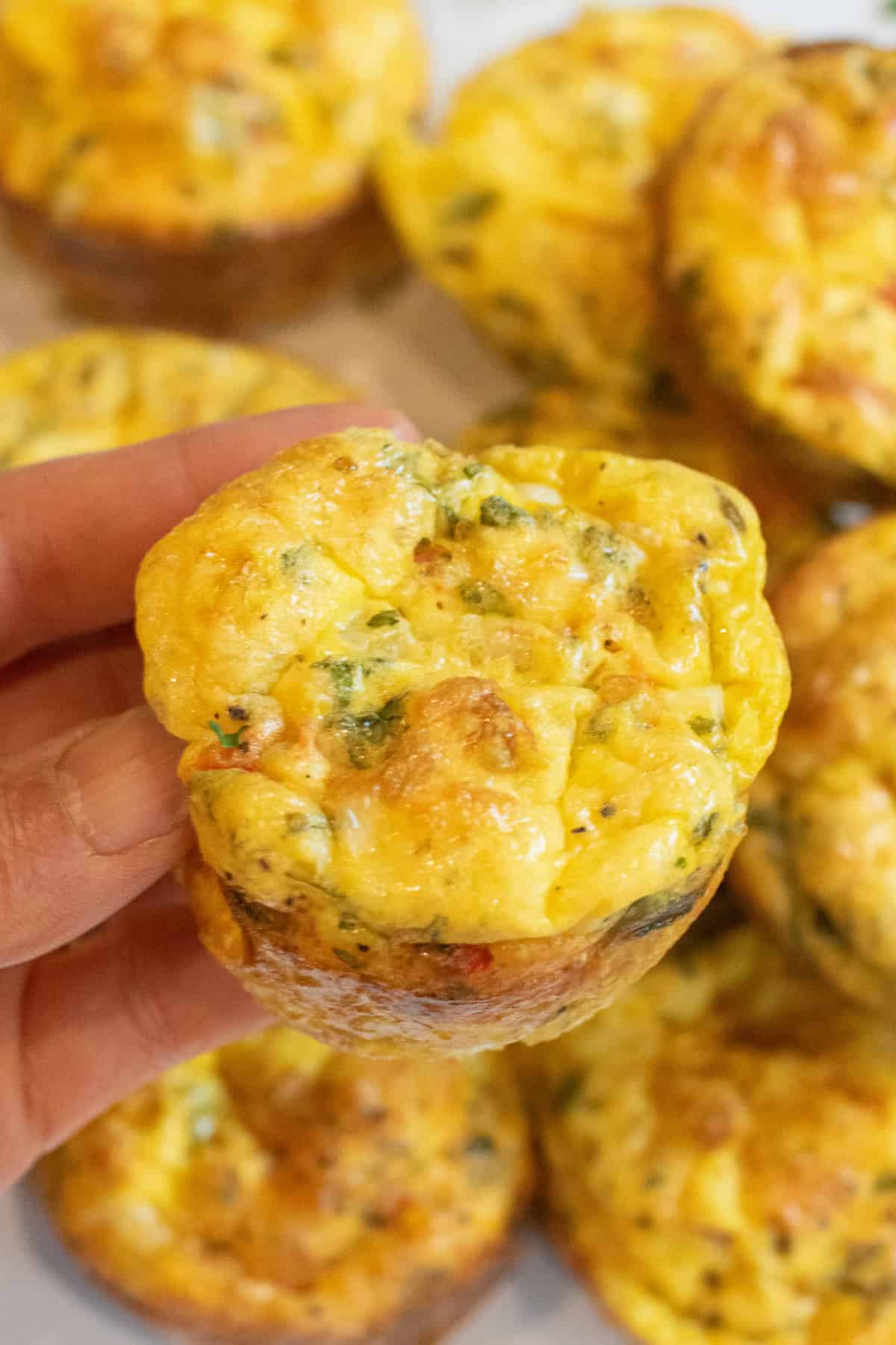 a hand holding an egg cup over a plate of baked egg cups.