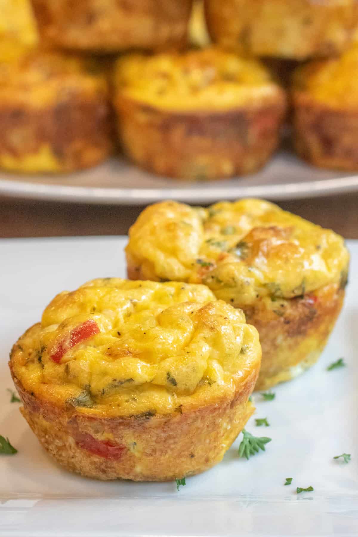 a plate of two baked egg cups in front of a large plate of more baked egg cups.
