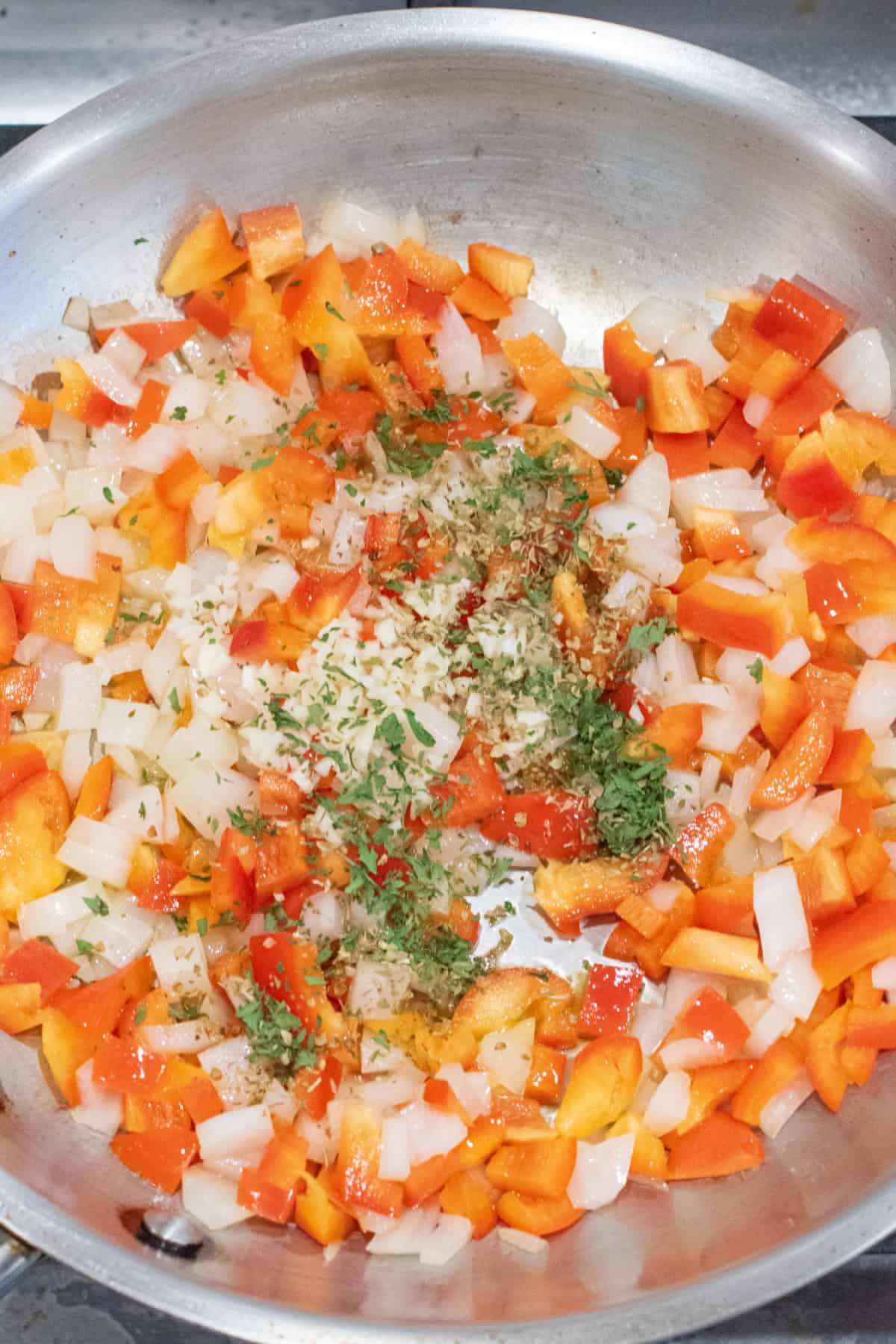 a saute pan with chopped bell pepper and onion and herbs.