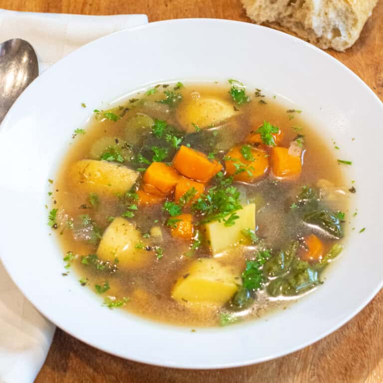 a bowl of soup with potatoes, carrots, and parsley.