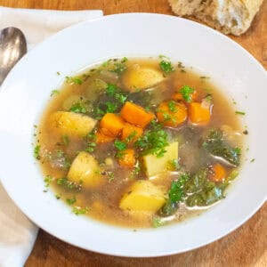 an overhead of a bowl of soup with potatoes, vegetables, and parsley.