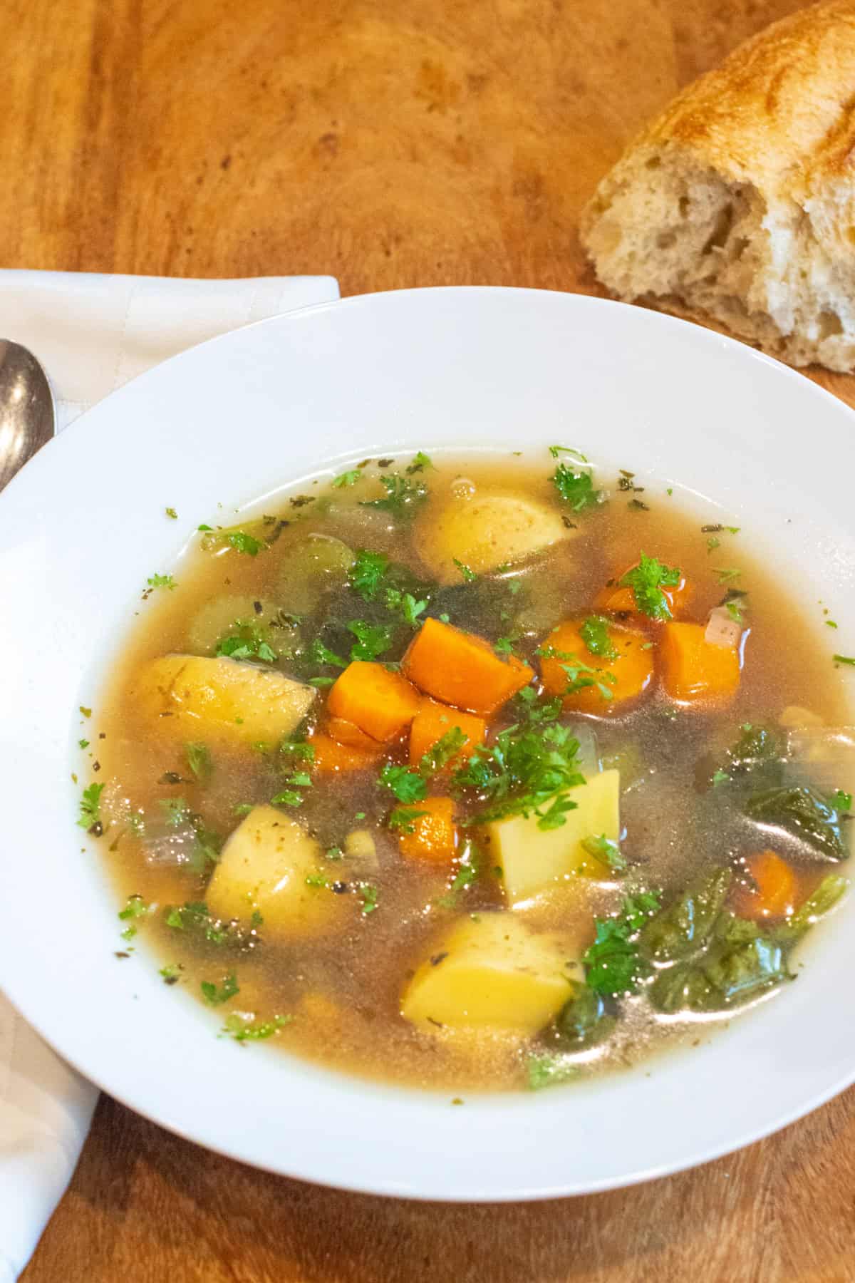 a bowl of soup with potatoes, carrots, and parsley.