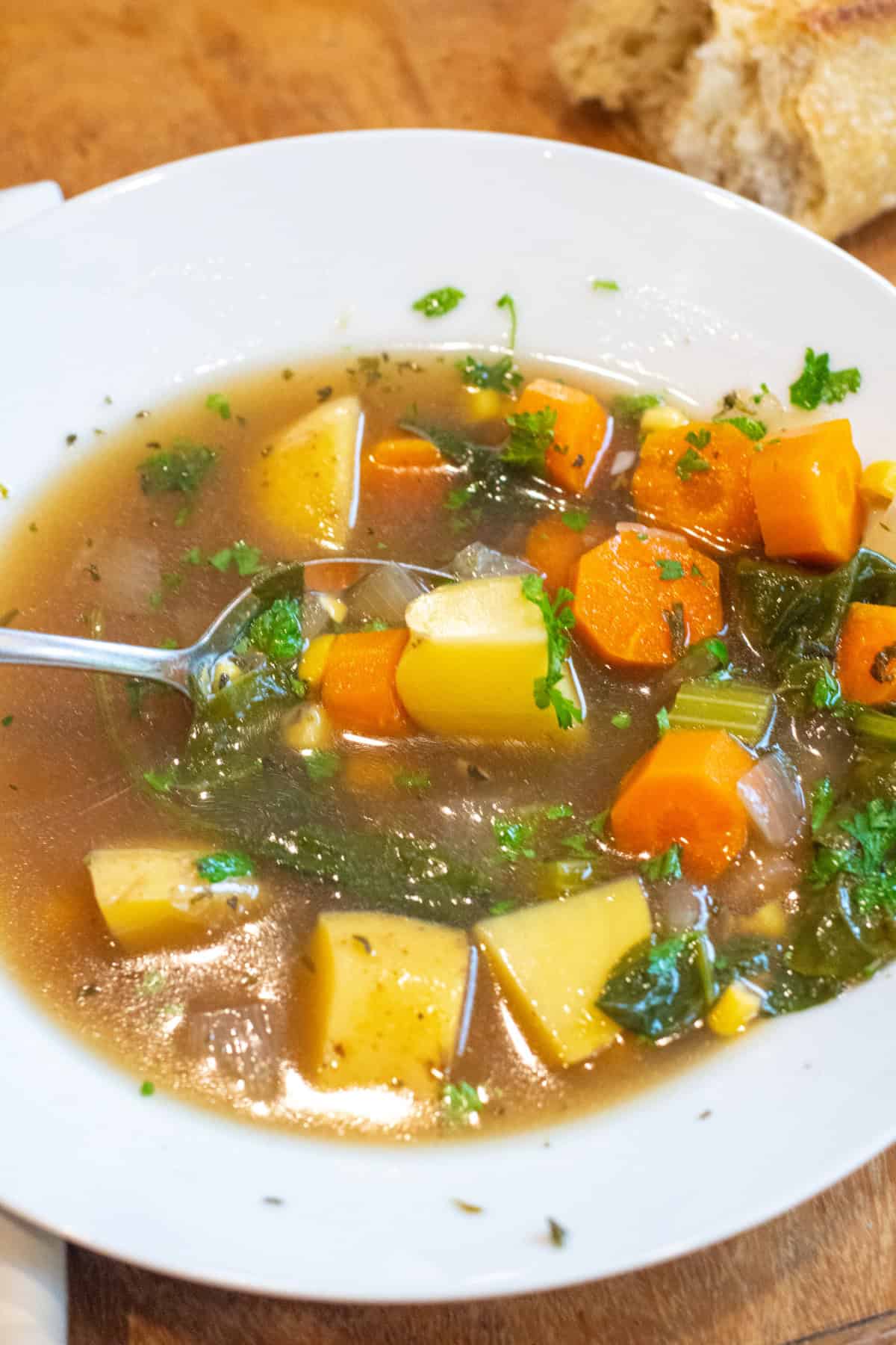 a bowl of soup with potatoes, carrots, and parsley with a spoon in it.