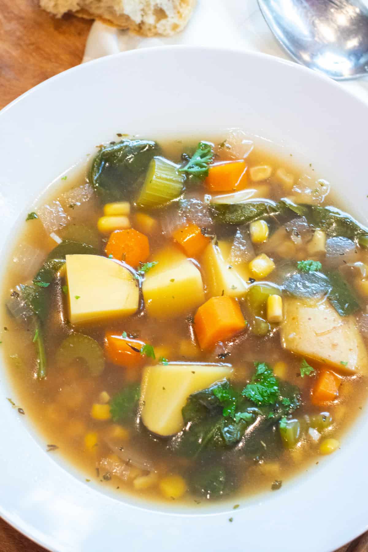 a bowl of soup with potatoes, carrots, and parsley with a spoon in it.
