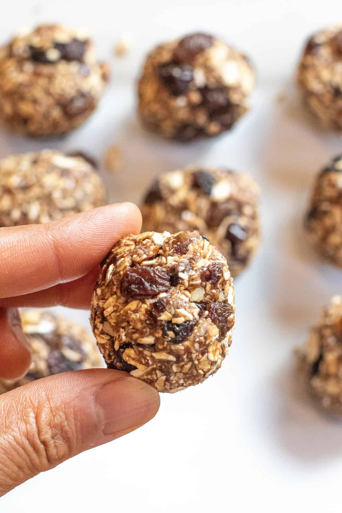 a plate of oat balls with raisins and a hand holding a ball between thumb and finger.