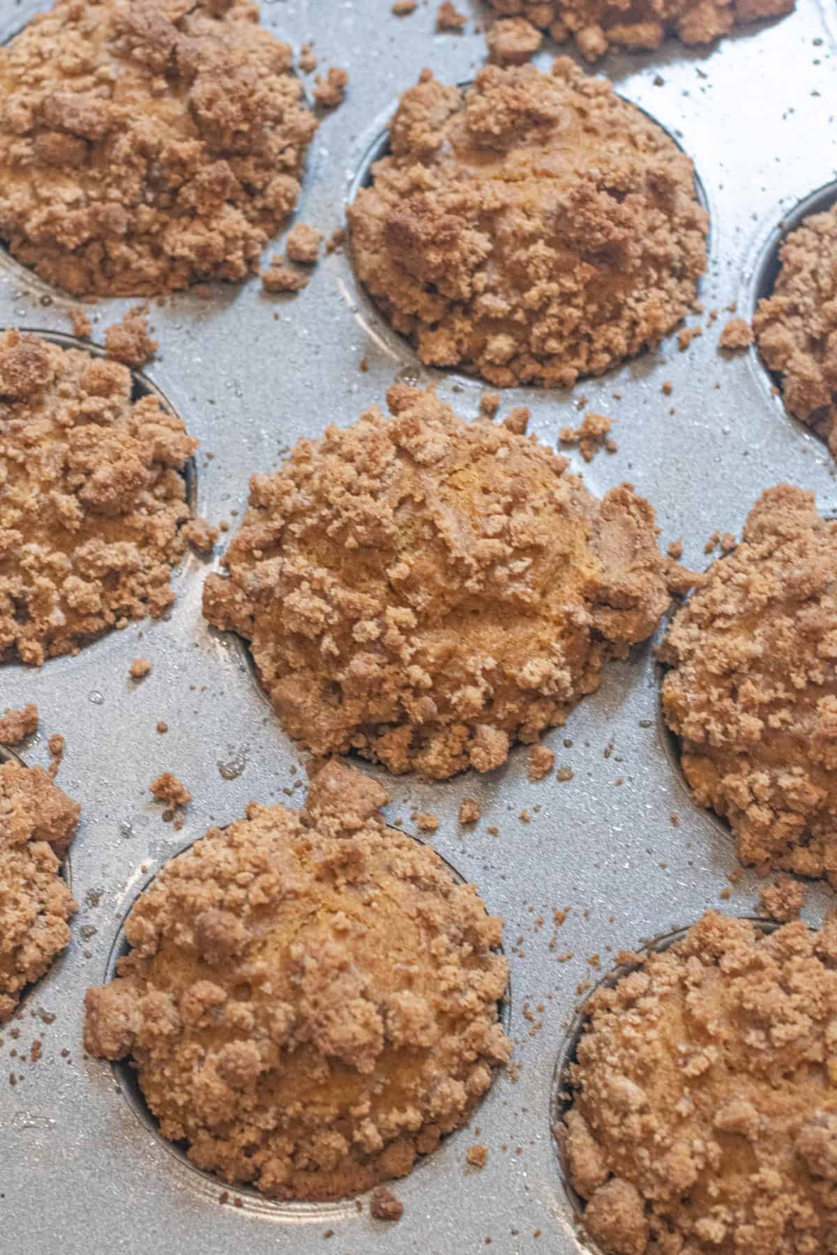 a muffin tray of baked muffins with a crumble on top.