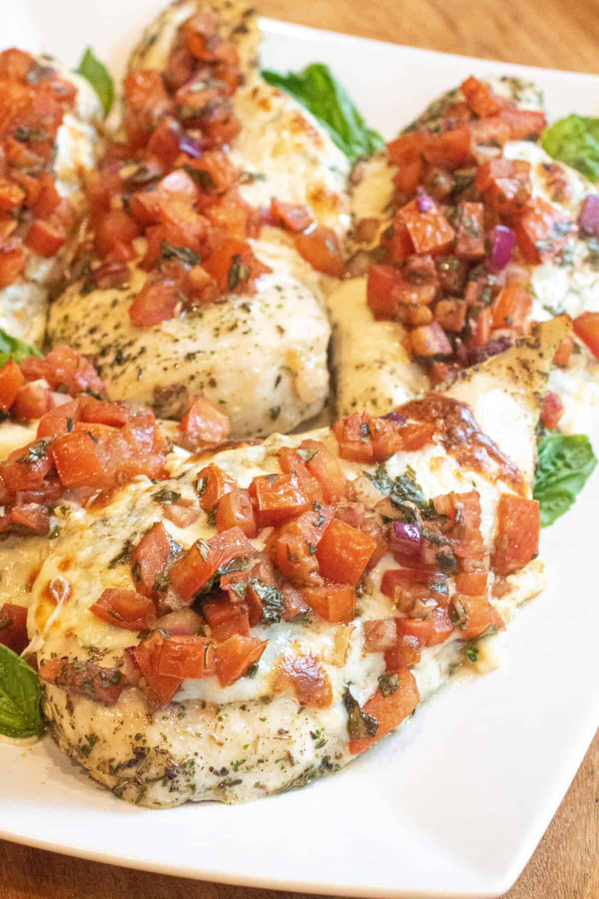 a plate of baked chicken breasts topped with melted cheese and tomato bruschetta.