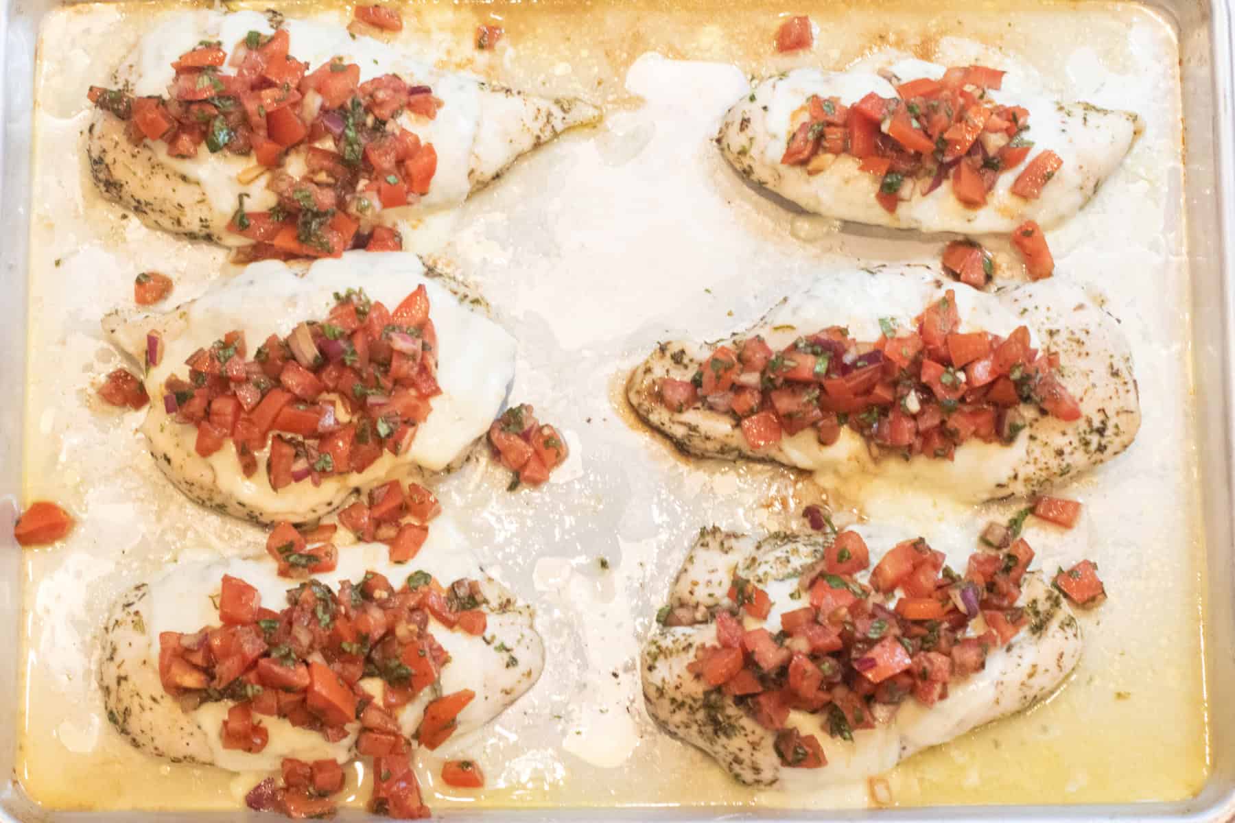 a tray with baked chicken topped with bruschetta.
