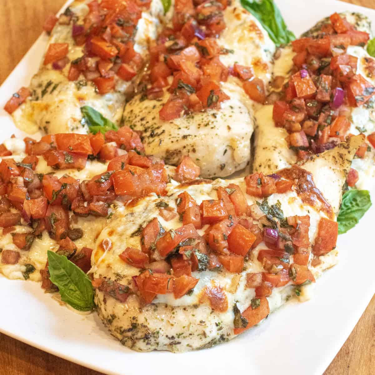 a plate of baked chicken breasts topped with melted cheese and tomato bruschetta.