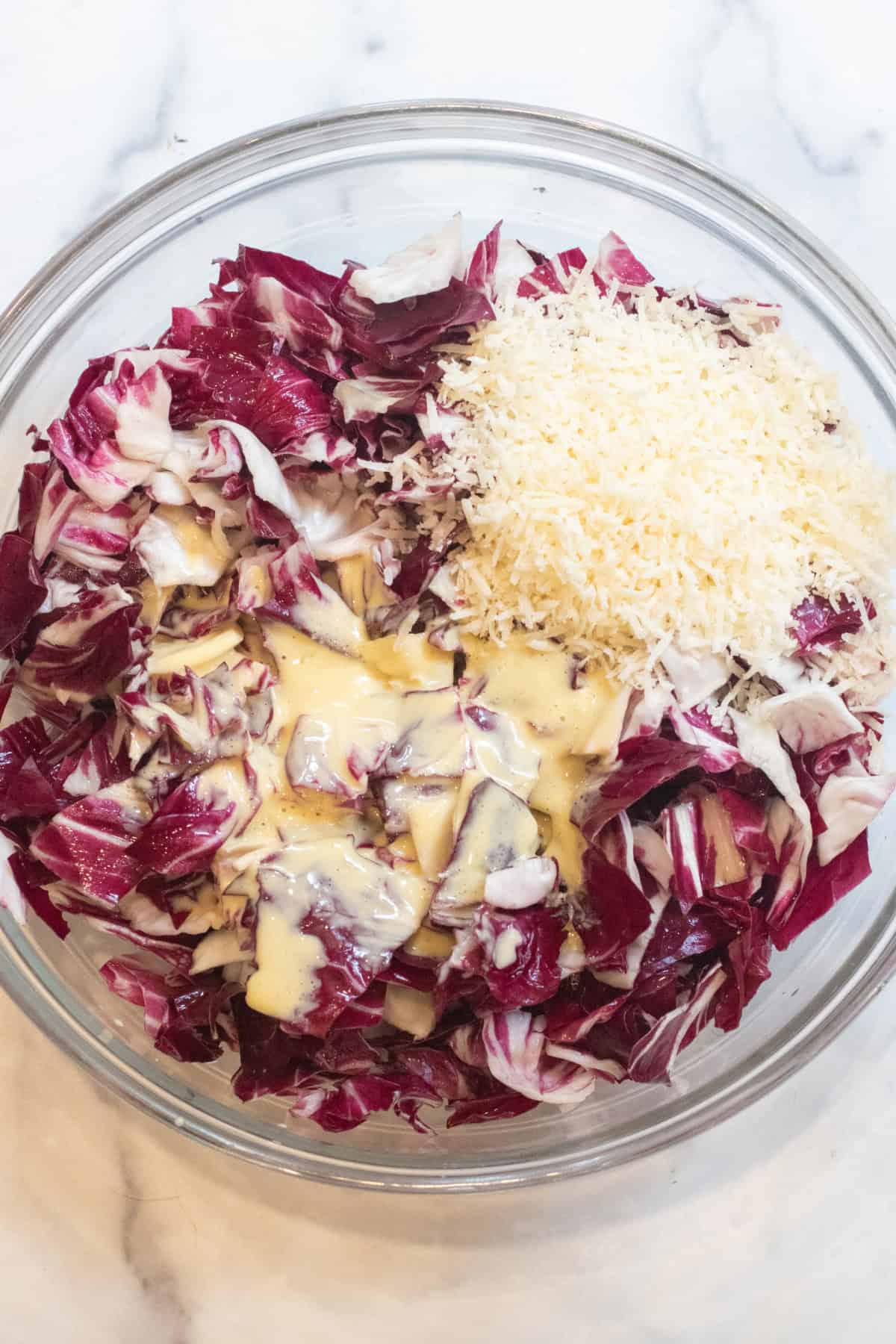 an overhead of a bowl of radicchio with dressing and grated cheese.